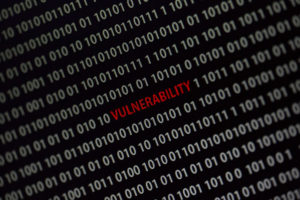Vulnerability' word in the middle of the computer screen surrounded by numbers zero and one. Image is taken in a small angle.