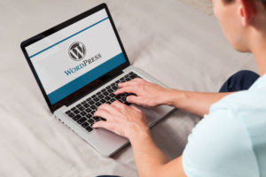 Wordpress brand logo on computer screen. Man typing on the keyboard.
