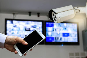 CCTV security camera monitor in office building and a man hand holding a smart phone.