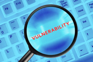 Magnifying glass on computer keyboard with "Vulnerability" word.