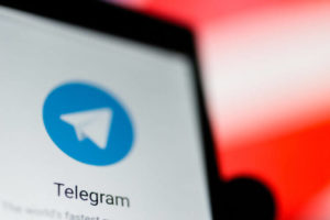 A mobile phone with the Telegram app in hand against a prohibiting sign.