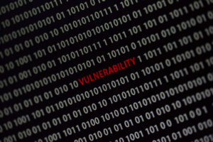 'Vulnerability' word in the middle of the computer screen surrounded by numbers zero and one. Image is taken in a small angle.