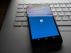 Facebook app on phone sitting on laptop with Facebook desktop site reflecting on screen.