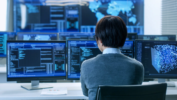 System Security Specialist Working at System Control Center. Room is Full of Screens Displaying Various Information.